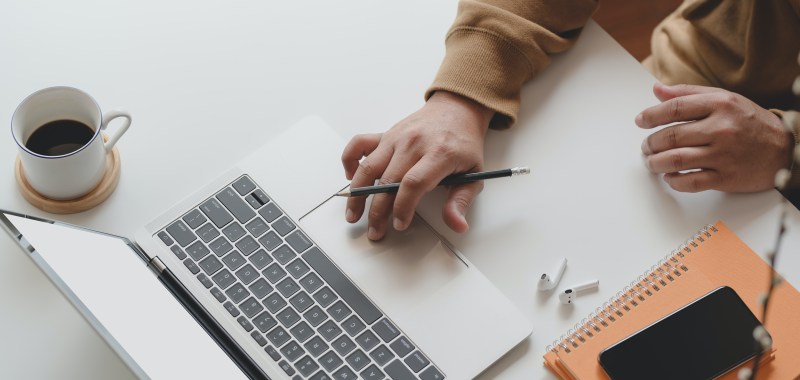 Hand gripping a pencil and using a laptop trackpad