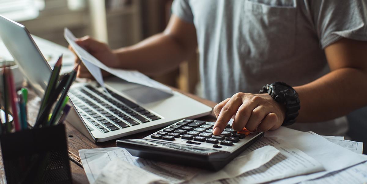 A person typing on a laptop with a calculator beside it.