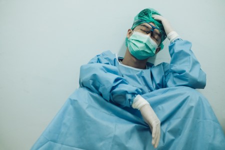 Exhausted surgeon sitting up against an interior wall
