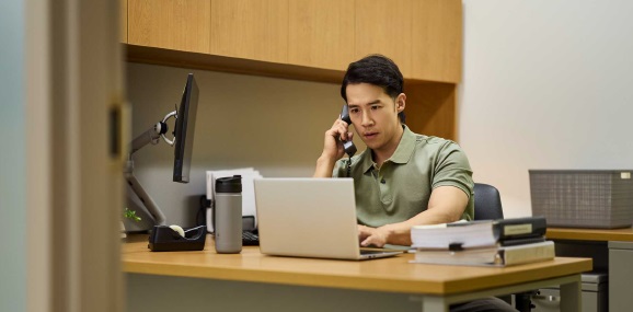 Physician at desk on both laptop and phone